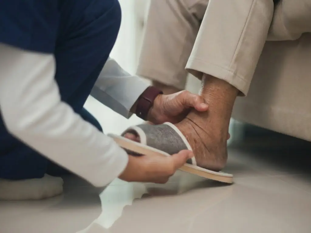 Caregiver in scrubs changing shoes of elderly person