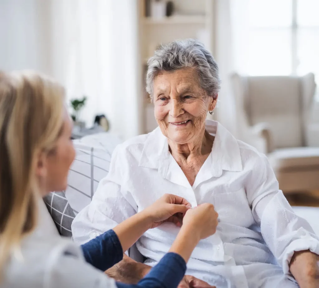 alumni home care caregiver buttoning elderly woman's shirt